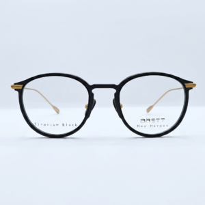 Black round eyeglasses with a black frame and gold accents at the temples, photographed against a light background.