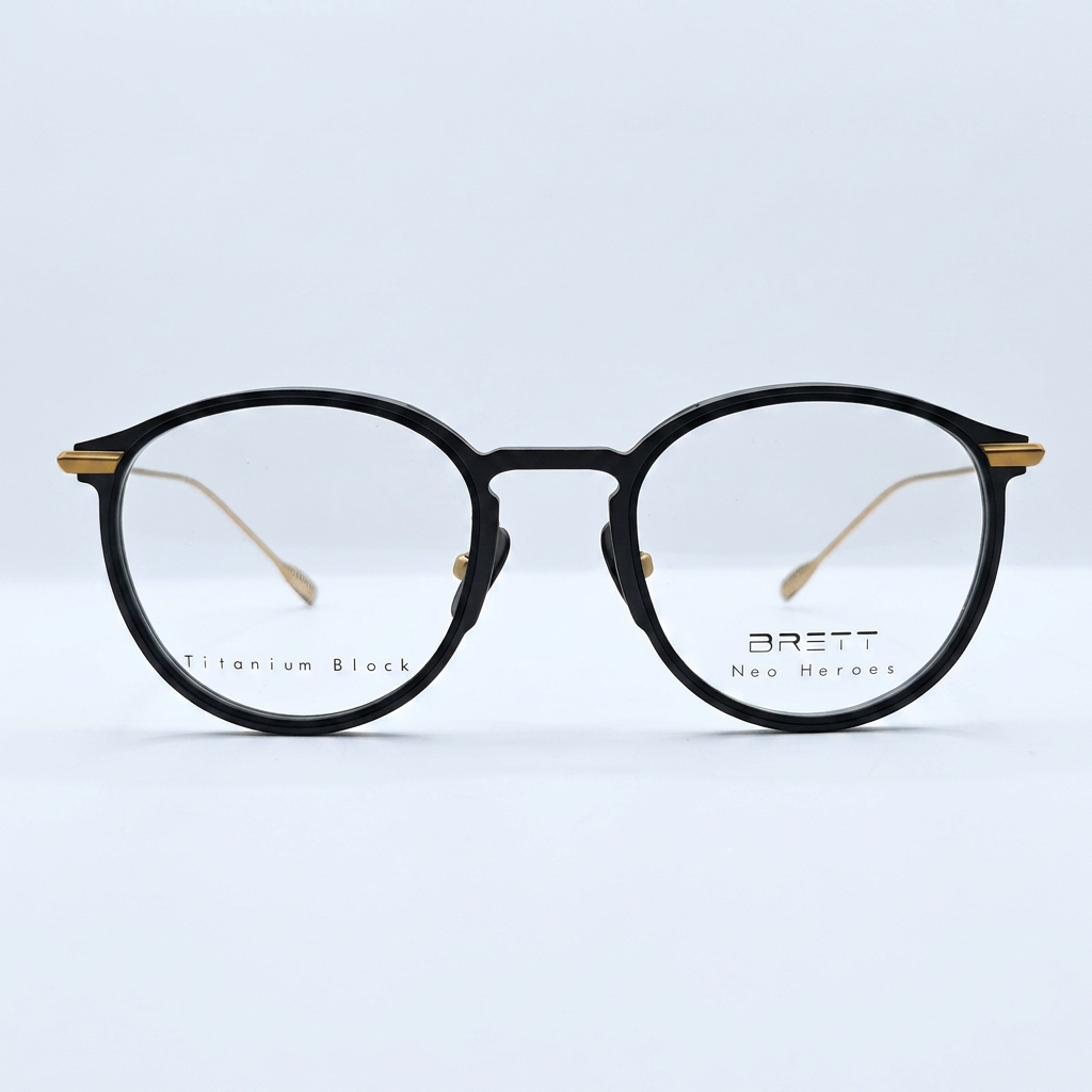 Black round eyeglasses with a black frame and gold accents at the temples, photographed against a light background.