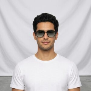 Portrait of a man with dark hair wearing aviator-style sunglasses and a white t-shirt, facing the camera against a light gray backdrop.