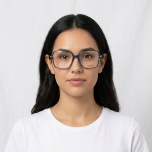 Portrait of a young woman with long dark hair wearing oversized blue-gray square glasses and a white t-shirt against a light background.
