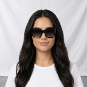Woman with long dark hair wearing oversized black sunglasses and a white t-shirt, facing the camera with a neutral expression.