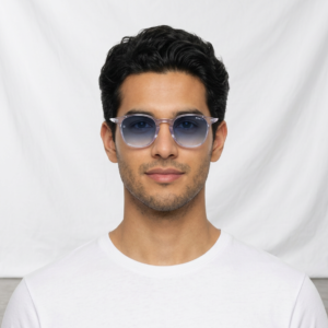 Portrait of a young man with short dark hair wearing translucent blue sunglasses and a white T-shirt, posed against a light backdrop.