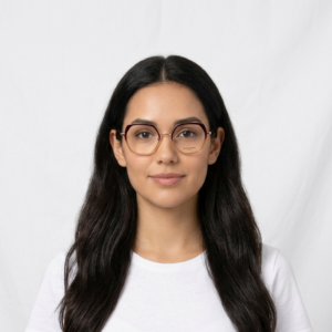 Portrait of a young woman with long dark hair, round glasses, and a white T-shirt against a plain white backdrop.